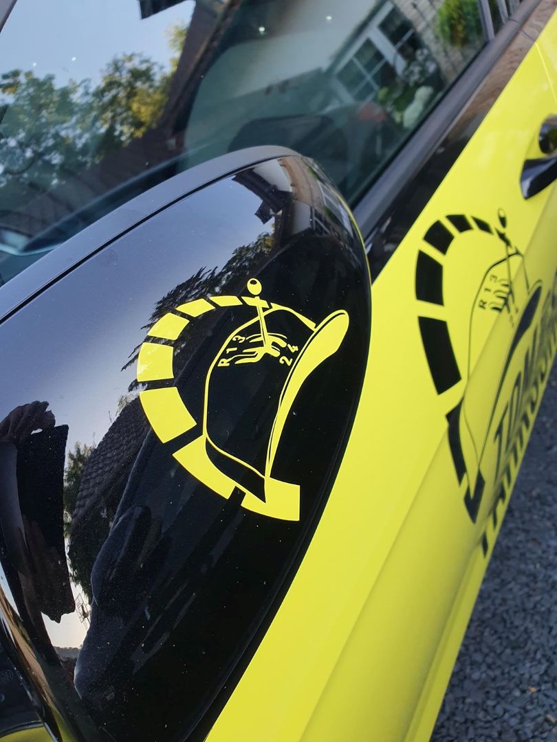 Zu sehen ist ein Seitenspiegel eines Fahrschulautos mit dem Logo der Fahrschule